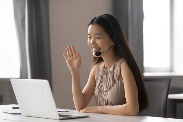 Lachende Aziatische zakenvrouw het dragen van draadloze headset zwaaiend doen video chat — Stockfoto