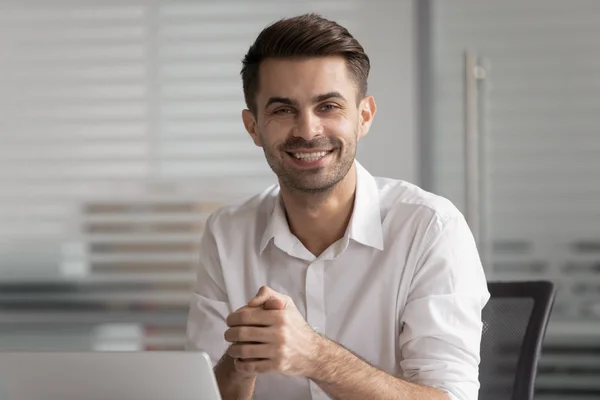 Homme d'affaires souriant assis au bureau avec un ordinateur portable regardant la caméra — Photo