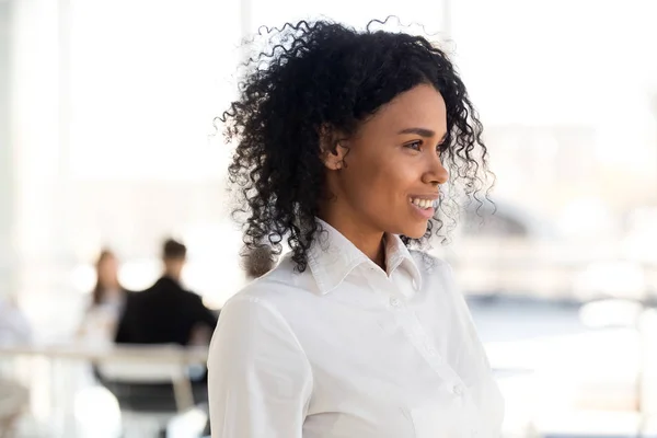 Sonriente mujer de negocios afroamericana mira a lo lejos, soñando —  Fotos de Stock