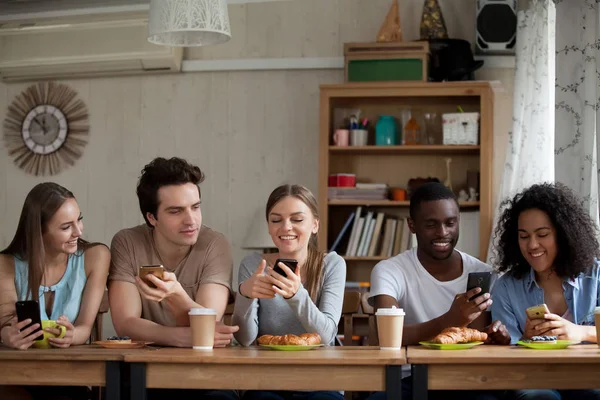 Leende olika unga kvinnor och män som använder smartphones i Café. — Stockfoto