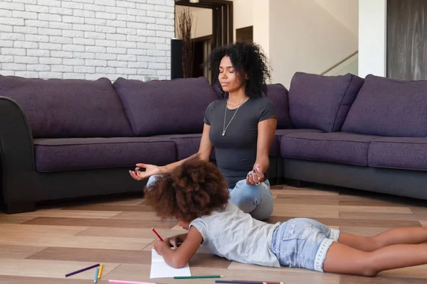 Afrikaanse moeder doen yoga terwijl haar dochter tekenen op de vloer — Stockfoto