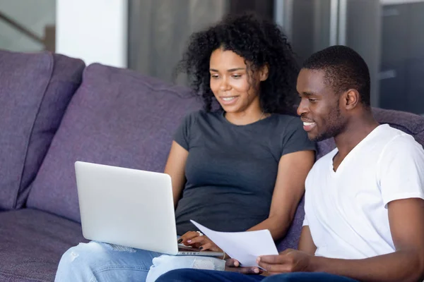 African couple sitting on couch checking bills using computer