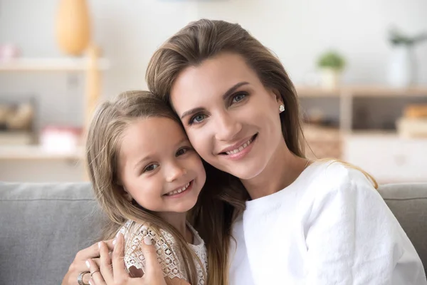 Beautiful mother and daughter sitting on couch looking at camera — Stock Photo, Image