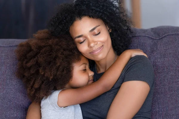 Closeup filha africana abraçando a mãe sentada no sofá em casa — Fotografia de Stock