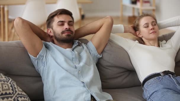 Pareja poniendo las manos detrás de la cabeza descansando en el sofá se siente bien — Vídeos de Stock
