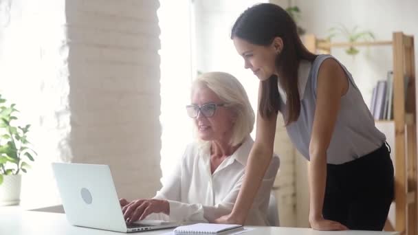 Leeftijd vrouwelijke mentor toont online app aan nieuwe werknemer meisje — Stockvideo