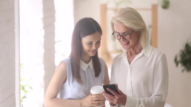 Diferentes edades colegas discuten nueva aplicación mirando la pantalla del teléfono inteligente — Vídeo de stock