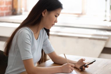 Konsantre Asyalı öğrenci akıllı telefon kullanarak notlar yapmak