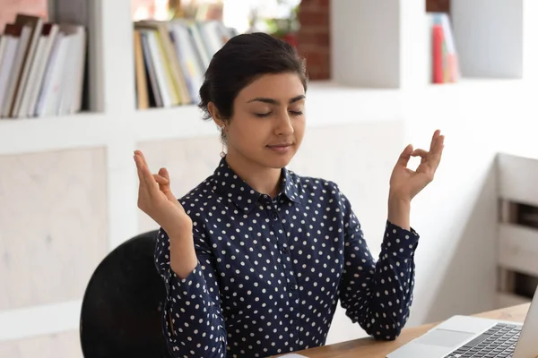 Concentrated indian girl meditating with closed eyes at workplace