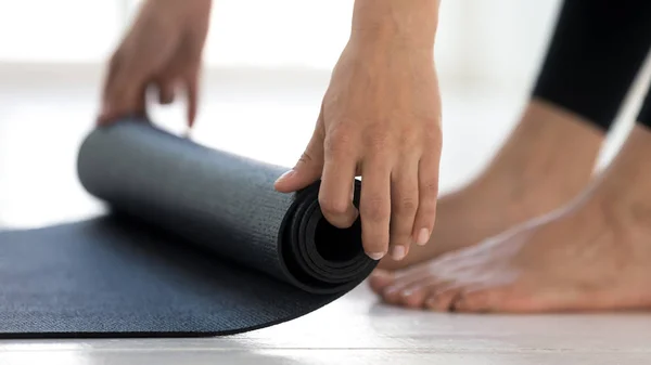 Menina desportiva rolando tapete de ioga preto antes ou depois do treino — Fotografia de Stock