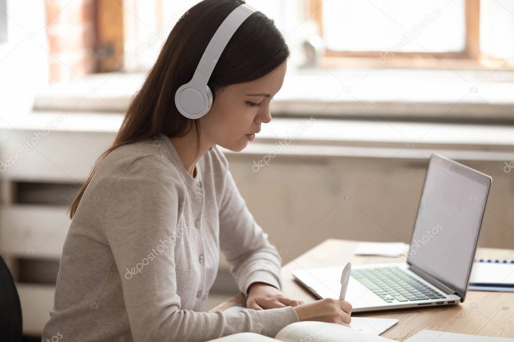 Female student doing homework listening to music in headphones