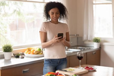 Mutfakta duran Afrikalı kadın cep telefonu kullanarak yemek pişirmekten rahatsız