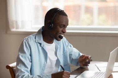 Afrikalı adam bilgisayar kullanarak online eğitim notları yapma kulaklık giymek