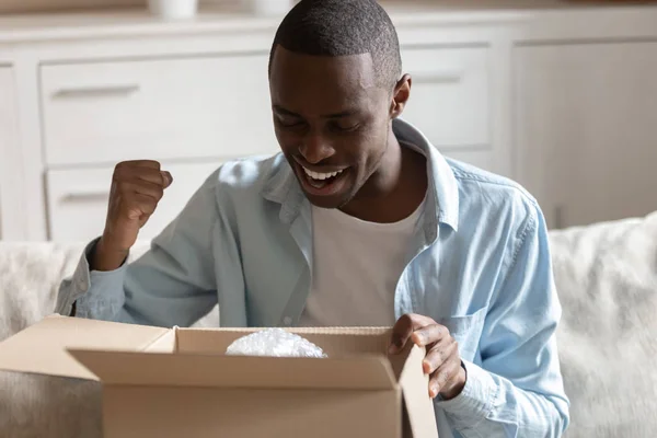 African guy looking inside carton box pleased with received parcel — Stock Photo, Image