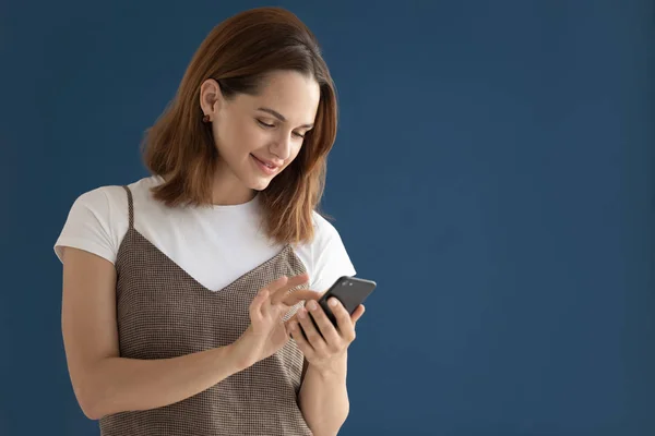 Mujer usando smartphone posando aislado sobre fondo de estudio azul oscuro —  Fotos de Stock