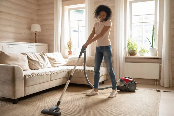 Mixed race woman vacuum cleaning carpet in living room — Stock Photo, Image