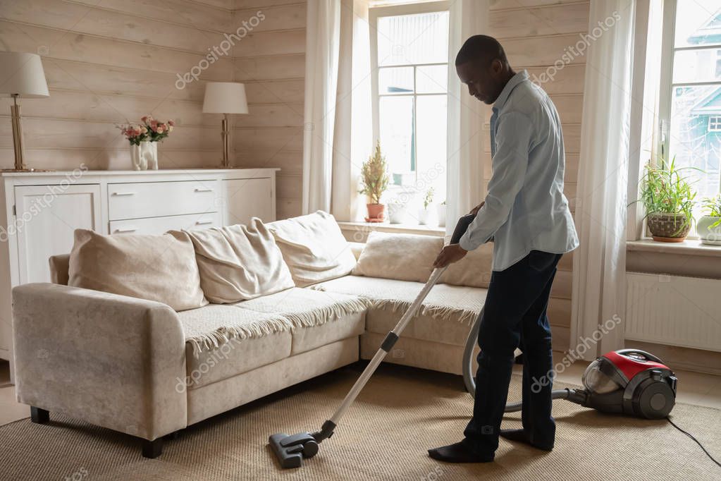 African guy use vacuum cleaner cleaning carpet in living room