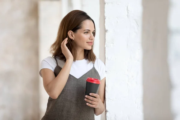 Mooie vrouw die papieren koffie kopje kijkt uit het raam — Stockfoto