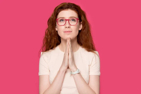 Sincere redhead woman holds hands together praying pose over pink — Stock Photo, Image