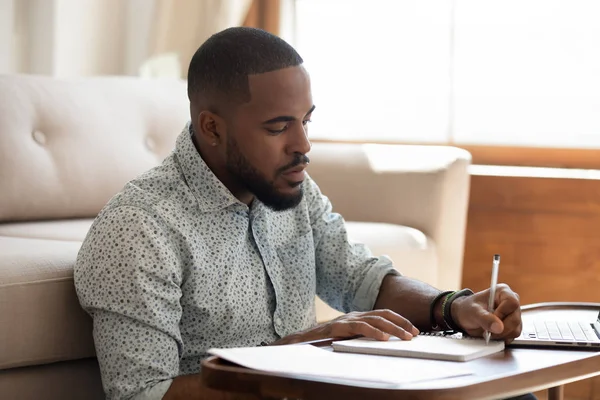 Allvarlig afrikansk student skriver anteckningar studera hemma med laptop — Stockfoto