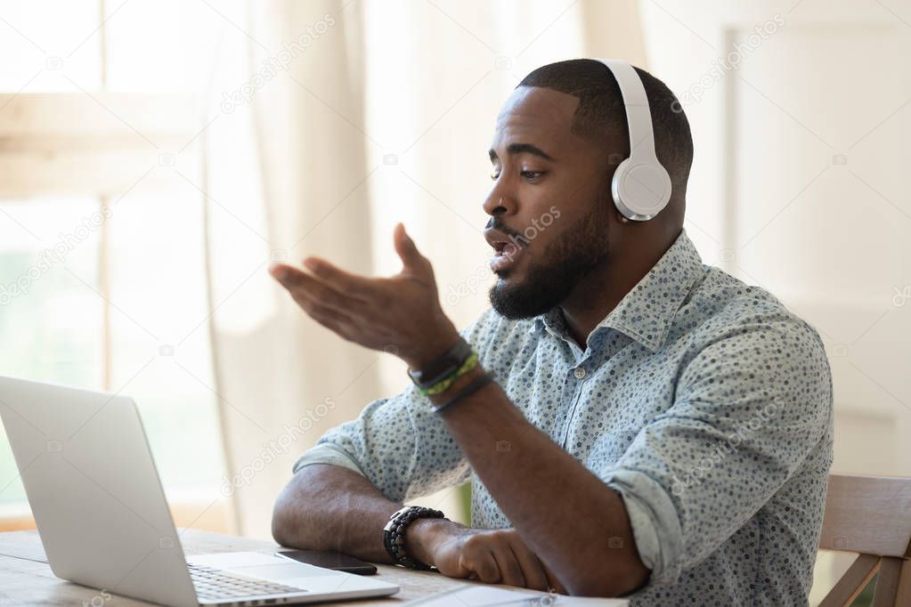 African male skype teacher wearing headphones talking looking at laptop