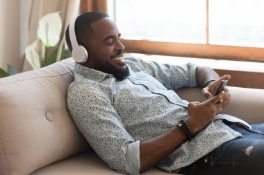 Akıllı telefondan müzik dinleyen kablosuz kulaklık takan rahat Afrikalı adam