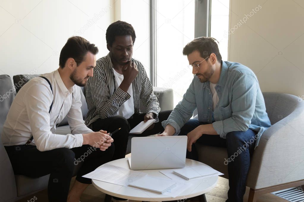 Three multiracial businessmen discuss online project look at laptop