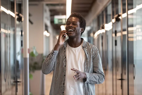 Happy black businessman talking on phone standing in office hallway