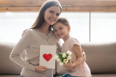 Mutlu küçük kızı buket ve kartpostal tutan minnettar anne kucaklayan