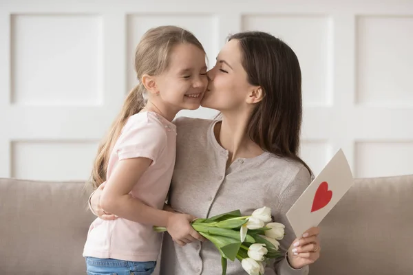 Matka całuje małą córkę wyrazić wdzięczność za kwiaty i pocztówkę — Zdjęcie stockowe
