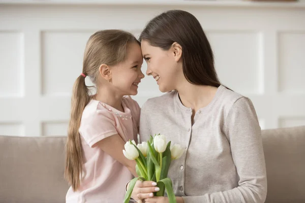Szczęśliwa matka trzyma białe tulipany dotyka czoła z córką — Zdjęcie stockowe