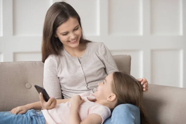 Daughter lying on mother laps spend time together using smartphone