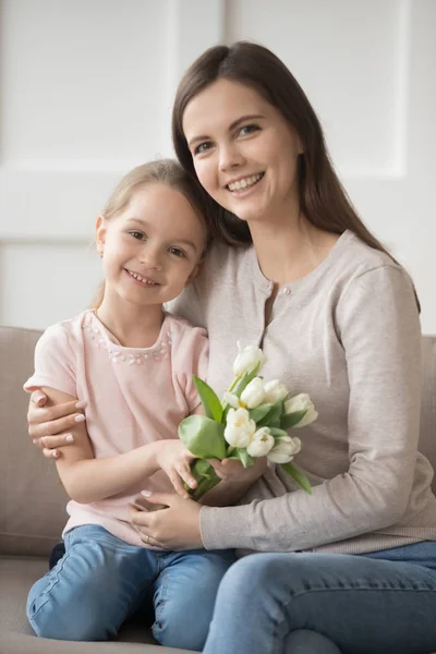 Daughter holding tulips sitting with mom on couch at home — Stock Photo, Image
