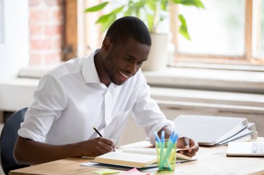 Gülümseyen Afrikalı öğrenci kalem tutan notlar test için hazırlanıyor