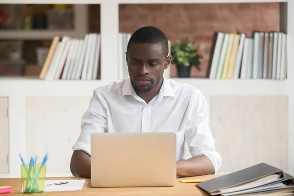 Poważny afrykański biznesmen siedzi przy biurku wpisując na komputerze — Zdjęcie stockowe
