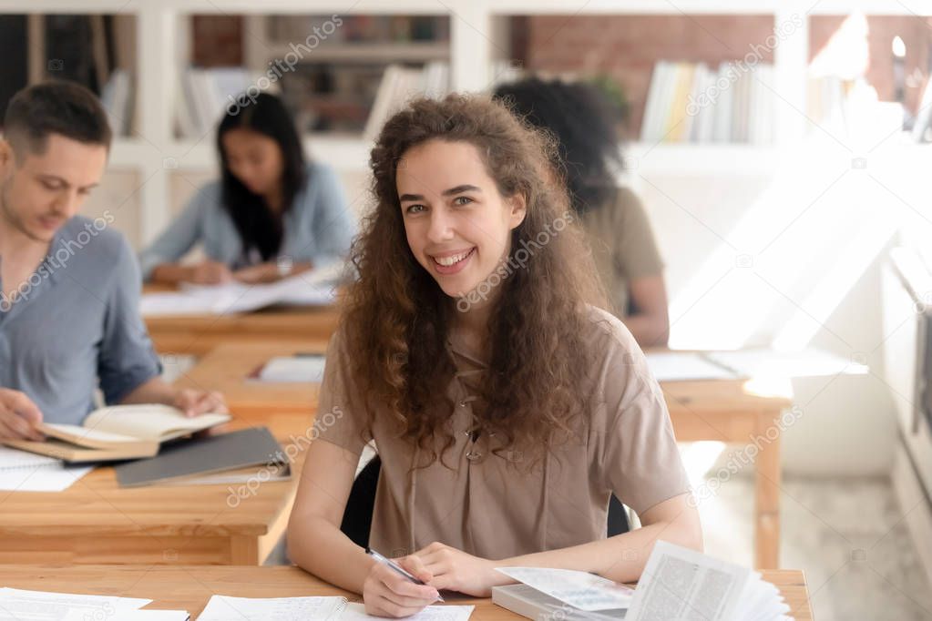 Successful university student sitting at desk looking at camera
