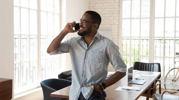 Happy african businessman standing in modern office talking on phone — Stock Photo, Image