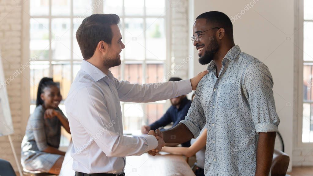 Happy black male employee get rewarded handshake proud white boss