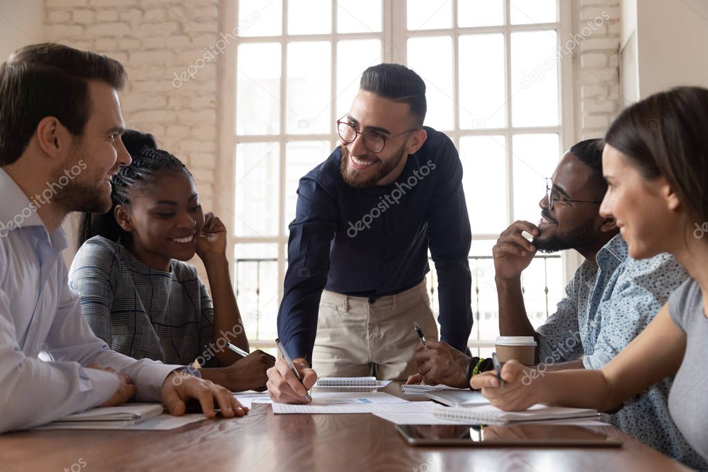 Smiling male leader and team discuss paperwork at group meeting