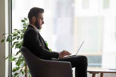 Ciddi işadamı büyük pencere yakınında dizüstü bilgisayar kullanarak gözlük giyiyor