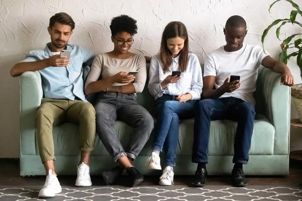 Multietniska unga människor sitter i rad med hjälp av mobiltelefoner — Stockfoto