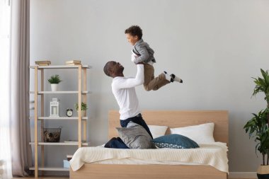 Mutlu siyah baba yatakta oynarken çocuk oğlu kaldırma tutarak