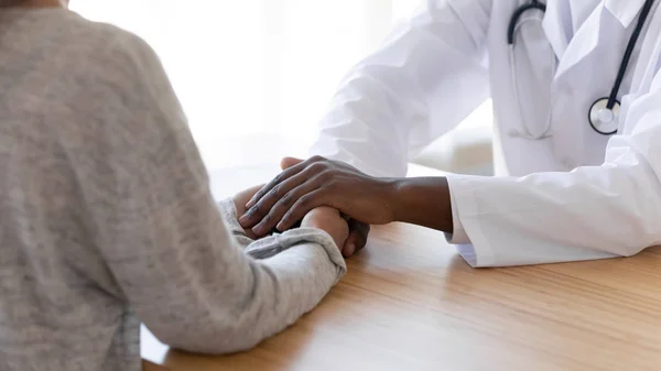 Black male doctor holding hands of female patient, closeup view