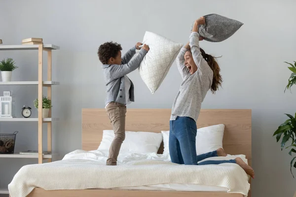 Mixed ethnicity mum and son enjoy pillow fight on bed