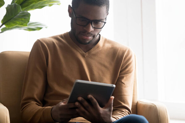 Focused African American man in glasses using tablet computer