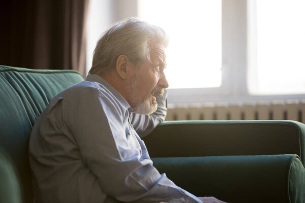 Thoughtful senior grandpa sit alone on sofa thinking of loneliness