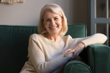 Kameraya bakan mutlu orta yaşlı kadın kanepeye oturun