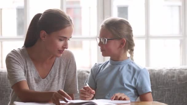 Joven madre ayuda con la tarea de la escuela a la pequeña hija — Vídeos de Stock