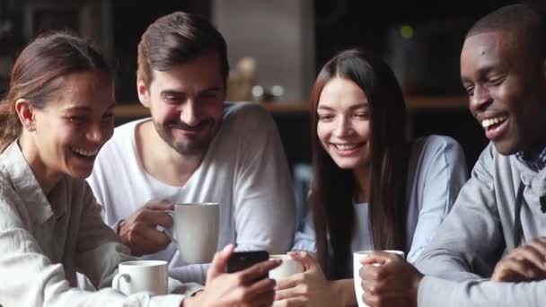 Diversos amigos se reunieron en la cafetería viendo videos divertidos en el teléfono inteligente — Vídeos de Stock