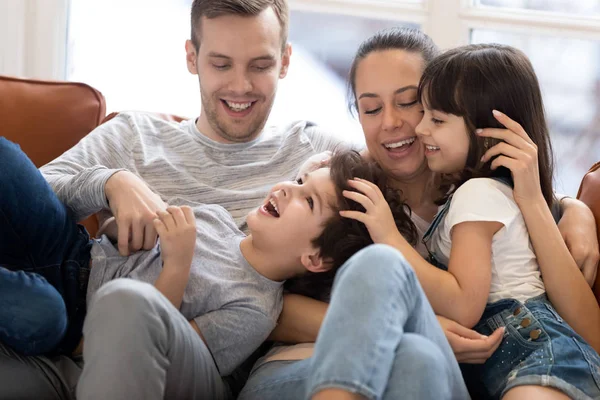 Счастливая мама папа веселится с детьми щекочет на диване — стоковое фото